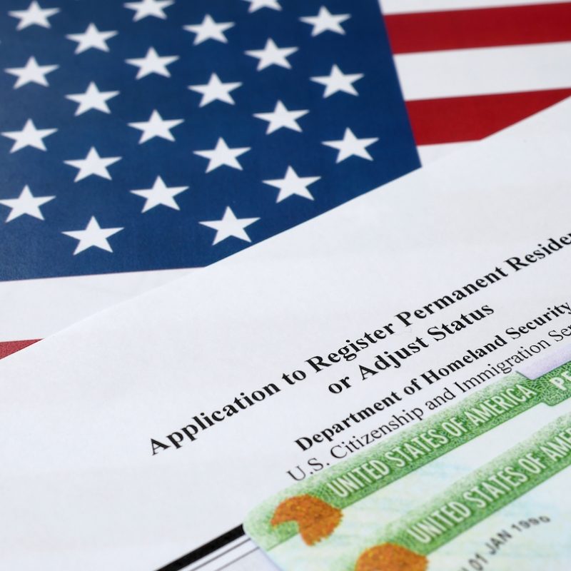 I-485 Application to register permanent residence or adjust status form and green card from dv-lottery lies on United States flag from Department of Homeland Security close up