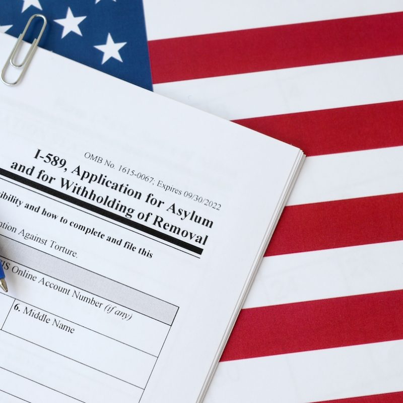 I-589 Application for asylum and for withholding of removal blank form lies on United States flag with blue pen from Department of Homeland Security close up